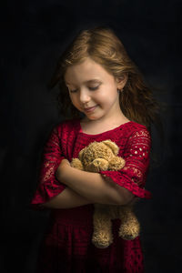 Cute smiling girl holding toy against black background