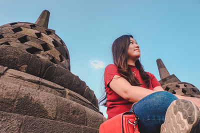Low angle view of woman sitting at stupas against blue sky