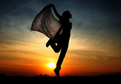 Silhouette woman with fabric jumping against sky during sunset