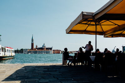 People at outdoors restaurant with church of san giorgio maggiore against clear sky