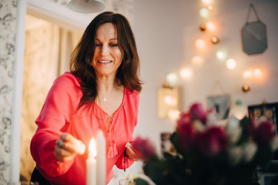 Happy mature woman igniting candle in party at home