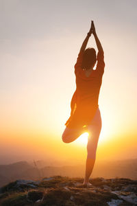 Woman stands in a yoga pose against the sun in the mountains, a silhouette of a sporty woman