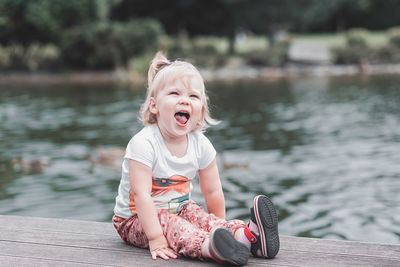 Cute girl sitting on pier against lake