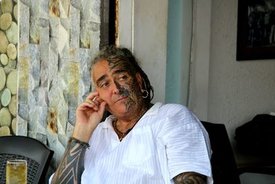 Thoughtful man with tattoo and pierced looking away by wall