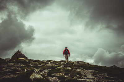 Rear view of man walking on mountain against cloudy sky