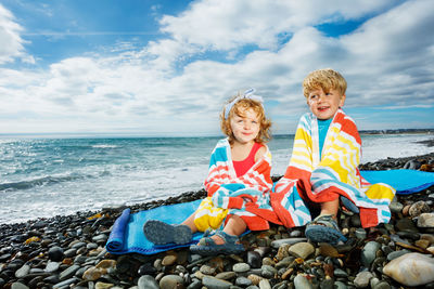 Side view of mother and daughter sitting on beach against sky