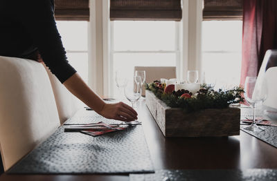 Close up of hand placing wine glass on place setting of dining table.