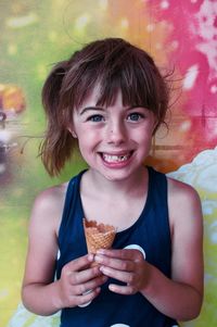 Close-up portrait of cute girl holding ice cream cone against wall