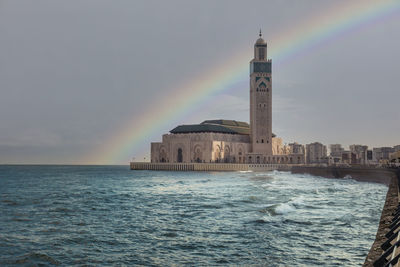 Scenic view of sea by building against rainbow in sky