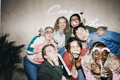 Happy multiracial male and female students with props against wall in college dorm