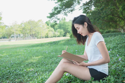 Young woman sitting on book against trees