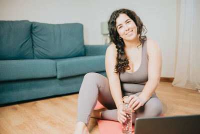 Smiling young woman with water bottle sitting at home