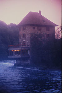 Building by river against sky at dusk