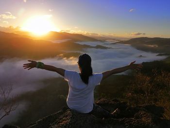 Rear view of woman with arms outstretched against sky during sunset