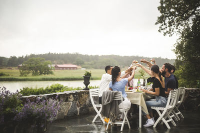 Male and female friends toasting drinks at dining table while spending weekend time in backyard