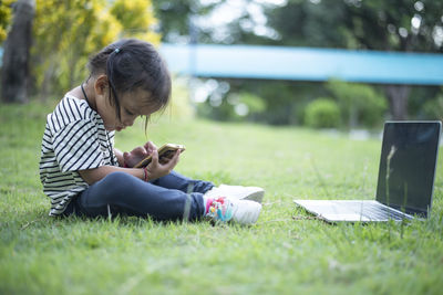 Young woman using mobile phone while sitting on field