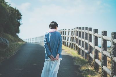 Rear view of woman walking on footpath against sky