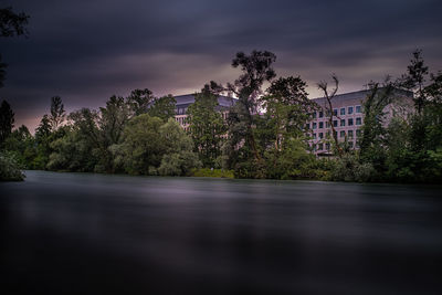 Plants and trees by lake against sky at dusk