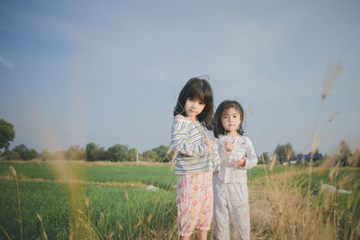 Portrait of cute sisters standing on grassy field against sky