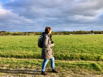 Side view of a woman walking along a green sunlit meadow under blue sky with clouds
