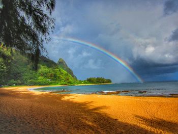 Low angle view of rainbow over sea against cloudy sky during sunny day