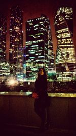 Woman standing against illuminated modern city at night