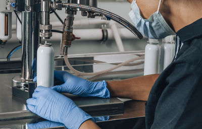 Unrecognizable woman in mask, cap, gloves works in production of cosmetics, pharmaceutical company