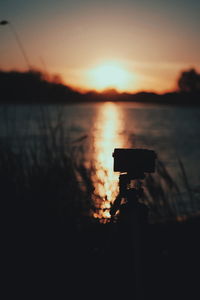 Silhouette of camera on lake against sky during sunset