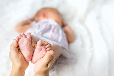 Girl holding feet of cute baby sleeping on bed at home