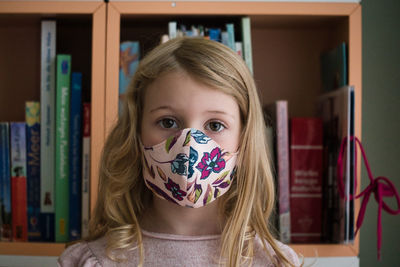 Close-up portrait of cute girl wearing mask standing at home