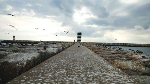 Lighthouse by sea against cloudy sky