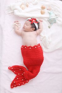 Directly above shot of baby girl wearing red mermaid costume sleeping on bed at home