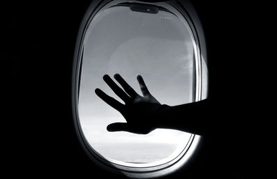 Close-up of silhouette hand against sky seen through window