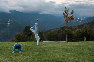 Rear view of mother and son performing yoga on mountain against sky