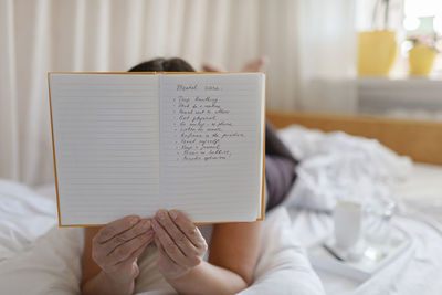 Midsection of woman reading book while sitting on bed