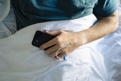 Patient holding mobile phone with iv drip hand lying on bed in hospital