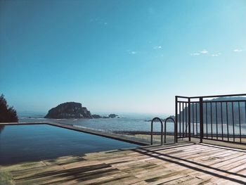 Scenic view of swimming pool by sea against clear blue sky