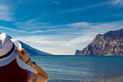 Woman wearing hat looking at lake against sky