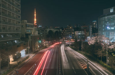 Light trails on city street by buildings against sky at night