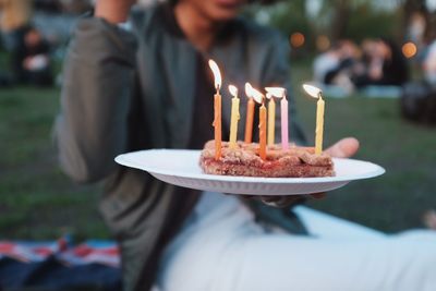 Midsection of person holding chocolate cake in plate at yard