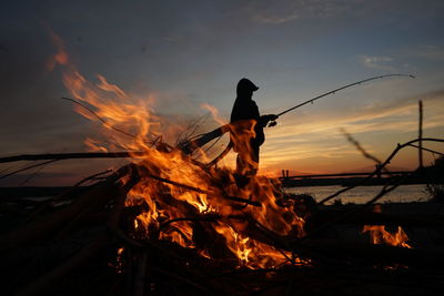 Silhouette of bonfire against sky at sunset