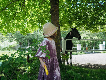 Small girl wearing lilac dress and summer hat looking at the horse