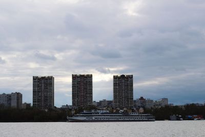 View of buildings by river against cloudy sky