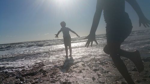 Silhouette people running on beach against sky