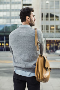 Rear view of businessman carrying shoulder bag on city street