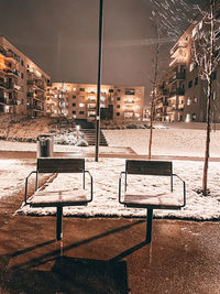 Empty benches and table by buildings in city