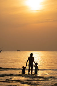 Silhouette mother with children standing in sea during sunset