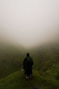 Rear view of man on landscape against sky during foggy weather