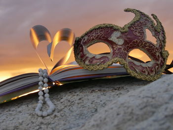 Low angle view of heart shape book pages with necklace and mask against sky during sunset