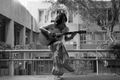 Woman playing guitar while sitting on railing